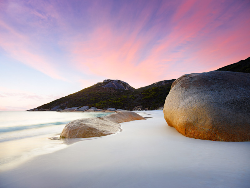 Rocks, sand, and the seashore against a bright red sunrise