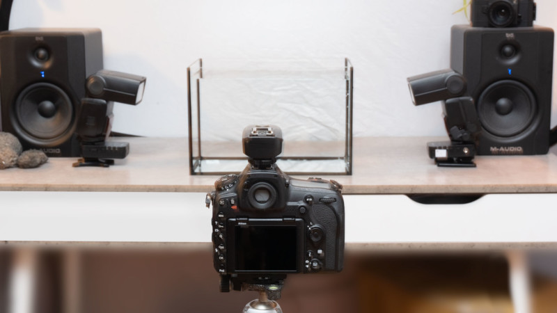 A Nikon D850 sits in front of the water tank and two speedlight flashguns