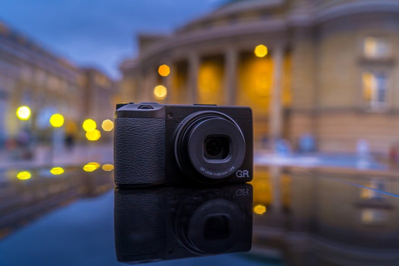 A Ricoh GR IIIx camera in front of a cityscape