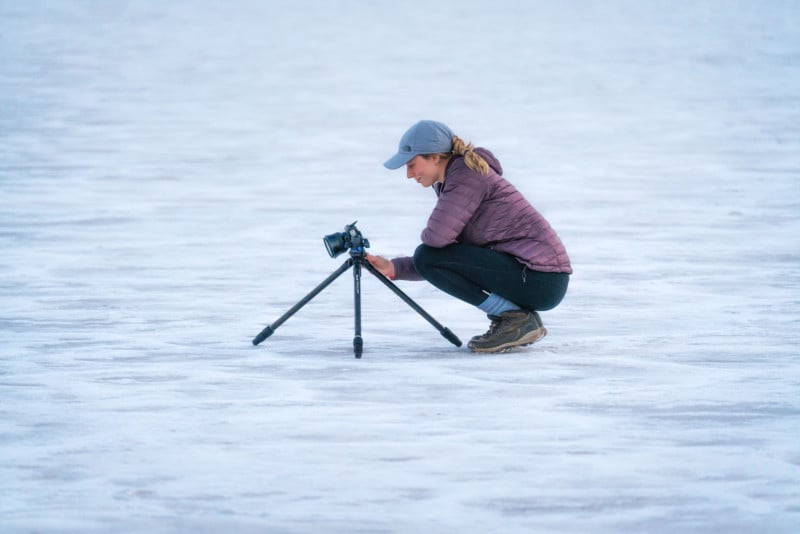 A woman setting up a camera and tripod in a snowy field