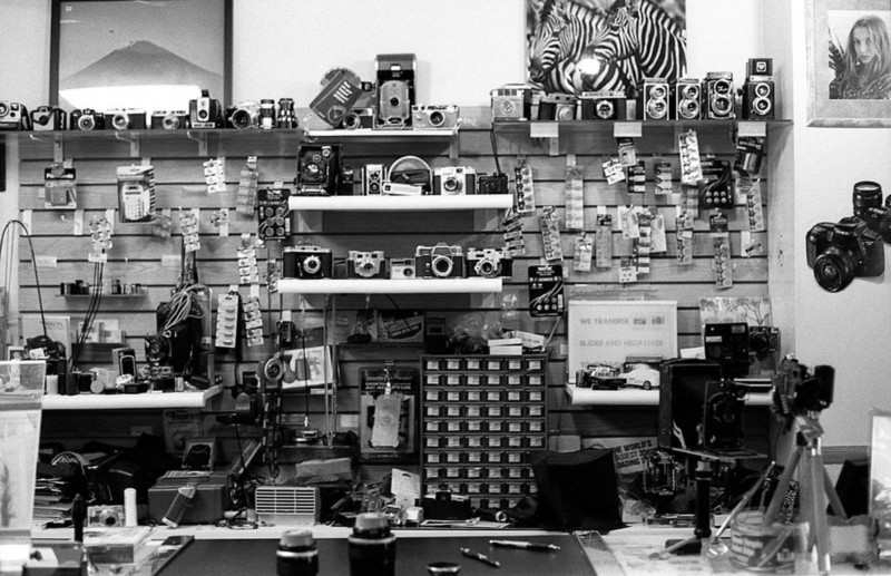 A view of a camera repair shop with vintage cameras on shelves and tools on a table