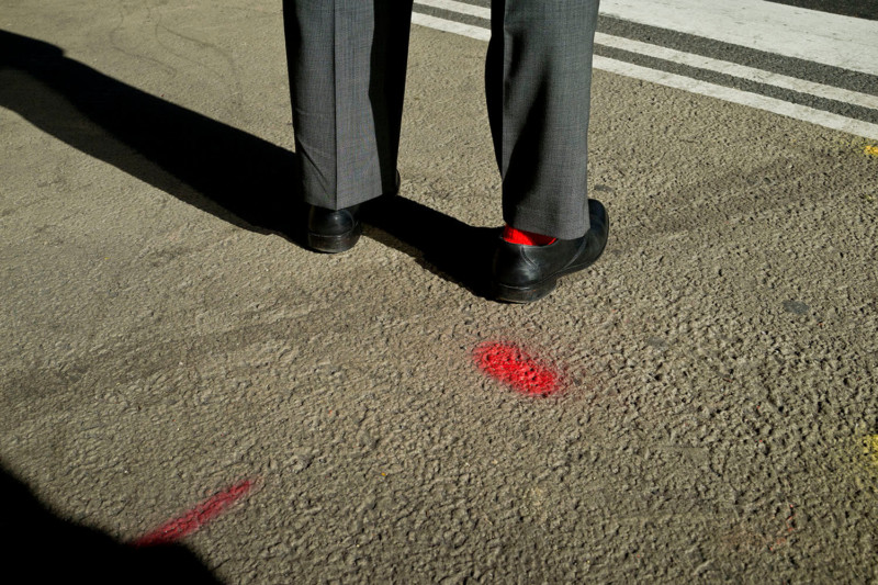 A man with a red sock standing next to a spot of red paint on the ground