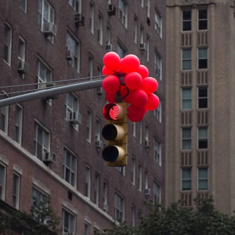 A traffic light with its red light illuminated covered with red balloons