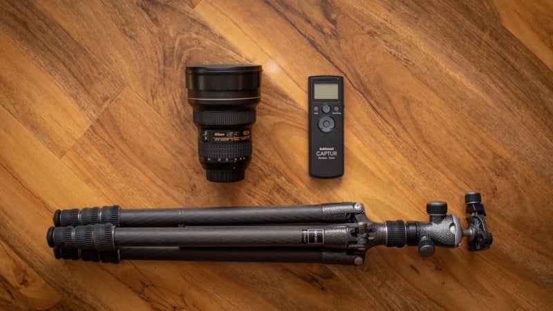 A flat lay image of a wide angle lens, intervalometer, and a tripod on a wooden floor