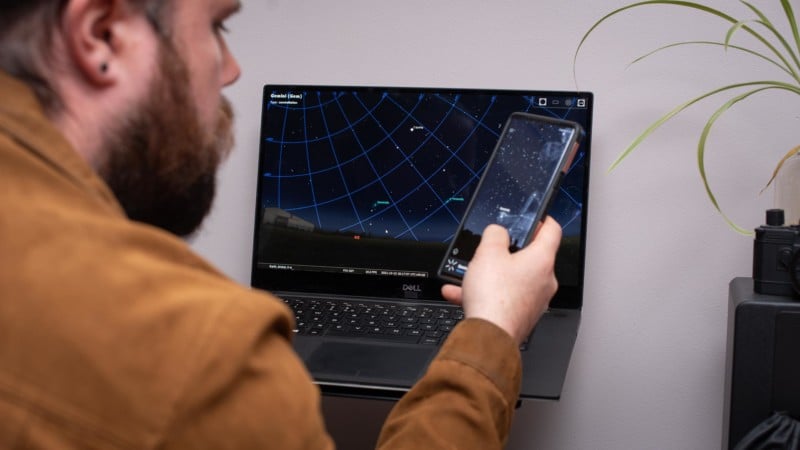 Person holding phone next to laptop with astro software on it