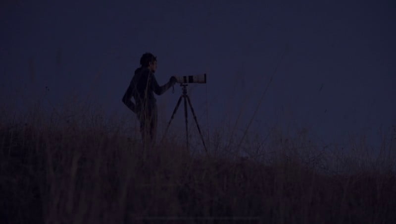 A man standing with a camera on a tripod at night