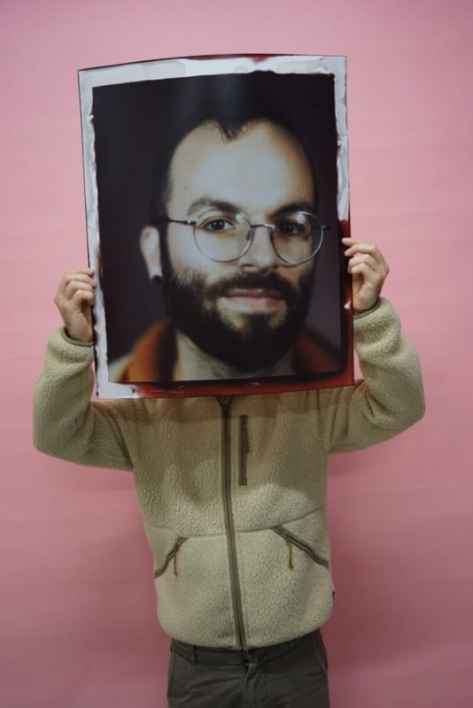 A man holding a giant 20 by 24 inch portrait of his face