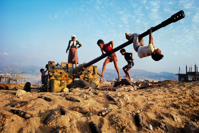 LEBANON-10001, Beirut, Lebanon, CAPTION: Children Play on Tank. Beirut, Lebanon, 1982. IG - 5.8.'17 Make-believe conquers the tools of war as children clamber over an abandoned anti-aircraft gun in Beirut, Lebanon, 1982. These tools of war became an improvised playground demonstrating the resilience of children. No matter how dire the situation, how dangerous the environment, children need to play. Whether it is splashing in puddles or climbing on abandoned tanks, their world of make believe is almost as important as food and shelter. MAX PRINT SIZE: 40x60 For children the detritus of war can function as an improvised playground. Derelict tanks, planes and military vehicles are often reclaimed as impromptu climbing frames. Yet, although the vehicle has been abandoned, an undercurrent of danger remains in the threat of numerous unexploded shells that litter the ground they play on. "The irony of children playing on an abandoned tank, as if it were a 'jungle gym' in a schoolyard. In this photograph, the scene is heightened by the explosive potential of the shells at the children's feet." - Phaidon 55 National Geographic, February 1983, Beirut: Up From the Rubble Magnum Photos, NYC9206, MCS1982003K008. Phaidon, 55, Iconic Images, final book_iconic Make-believe conquers the tools of war as children clamber over an abandoned antiaircraft gun. Discarded shells around the gun may still be live, like the explosive grievances and vengeance harbored by many of Beirut's factions. Will there at least come a consensus that a time to bomb must give way to a time to rebuild? Ellis, William S. (February 1993_. Beirut -Up From the Rubble. National Geographic, Vol. 163, No. 2,284 Steve Mccurry_Book final print_MACRO final print_milan final print_Birmingham final print_HERMITAGE Graphic Novel_book Bonnie Book FINAL SELECT retouched_Sonny Fabbri, Sam Wallander 5/26/2018