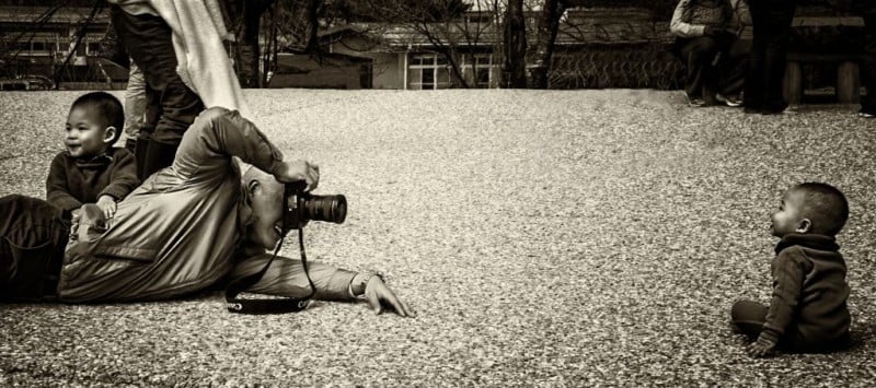 A man lying down to photograph a child