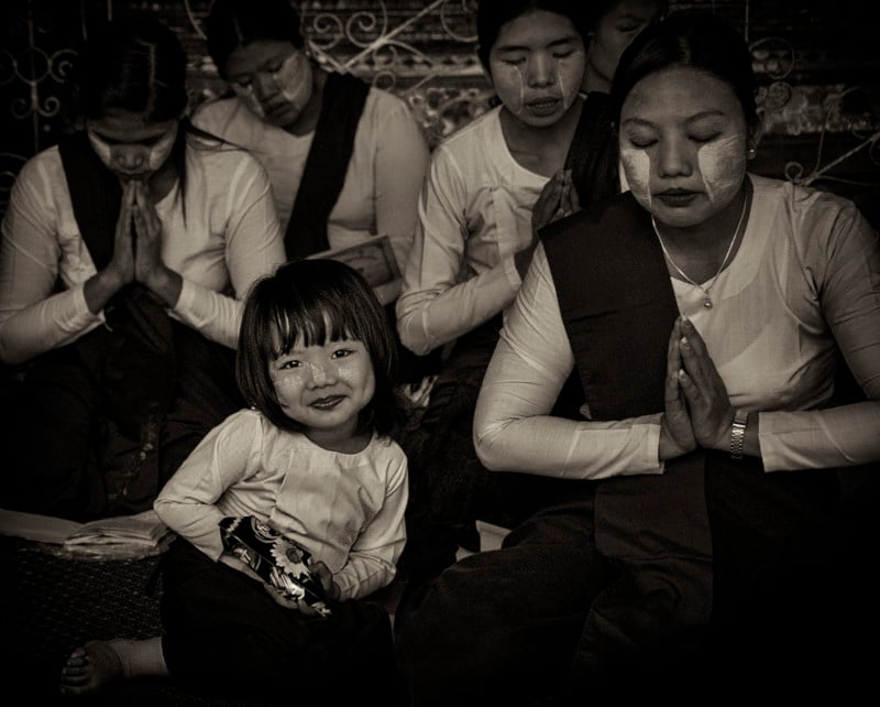 A little girl smiles while women around her pray