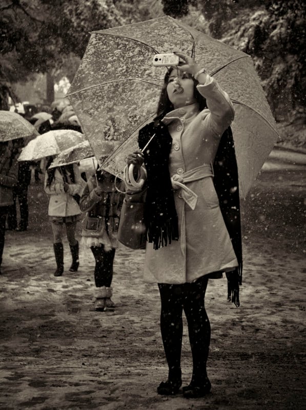 A woman holding an umbrella in snowfall while shooting a photo