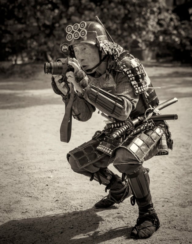 A man wearing Japanese samurai armor crouching to shoot a photo with a camera