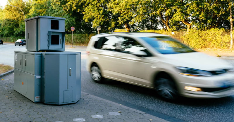 A speed camera on the side of the road in Germany with a car driving past