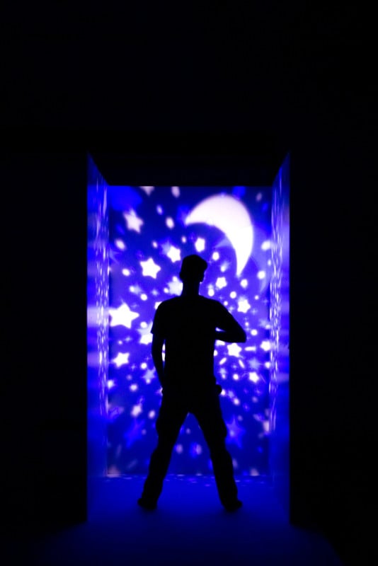 The silhouette of a man with stars and the moon projected on the wall behind him