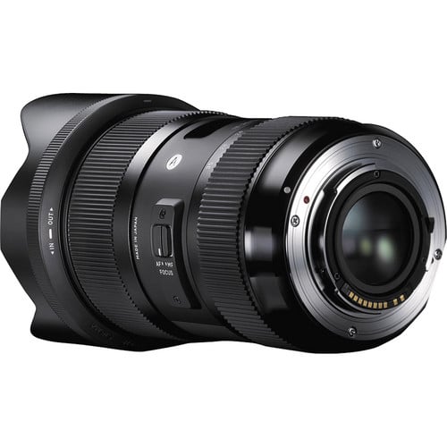 A close-up view of a black camera lens, showing the rear mount, focus and zoom rings, and lens switches, with metallic electronic contacts visible on the mounting end.