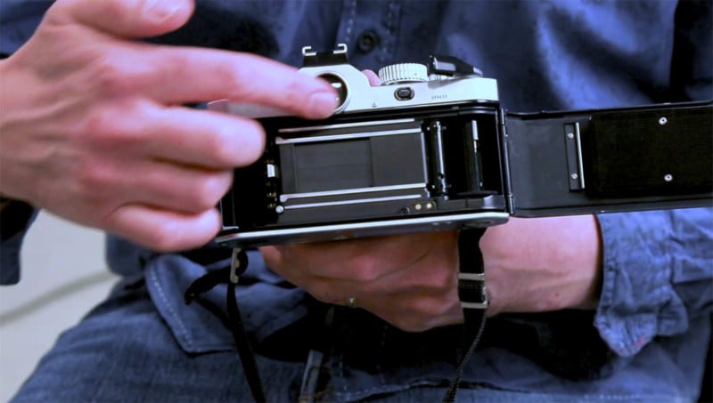 A photographer showing the inside of a 35mm film camera with its mechanical shutter