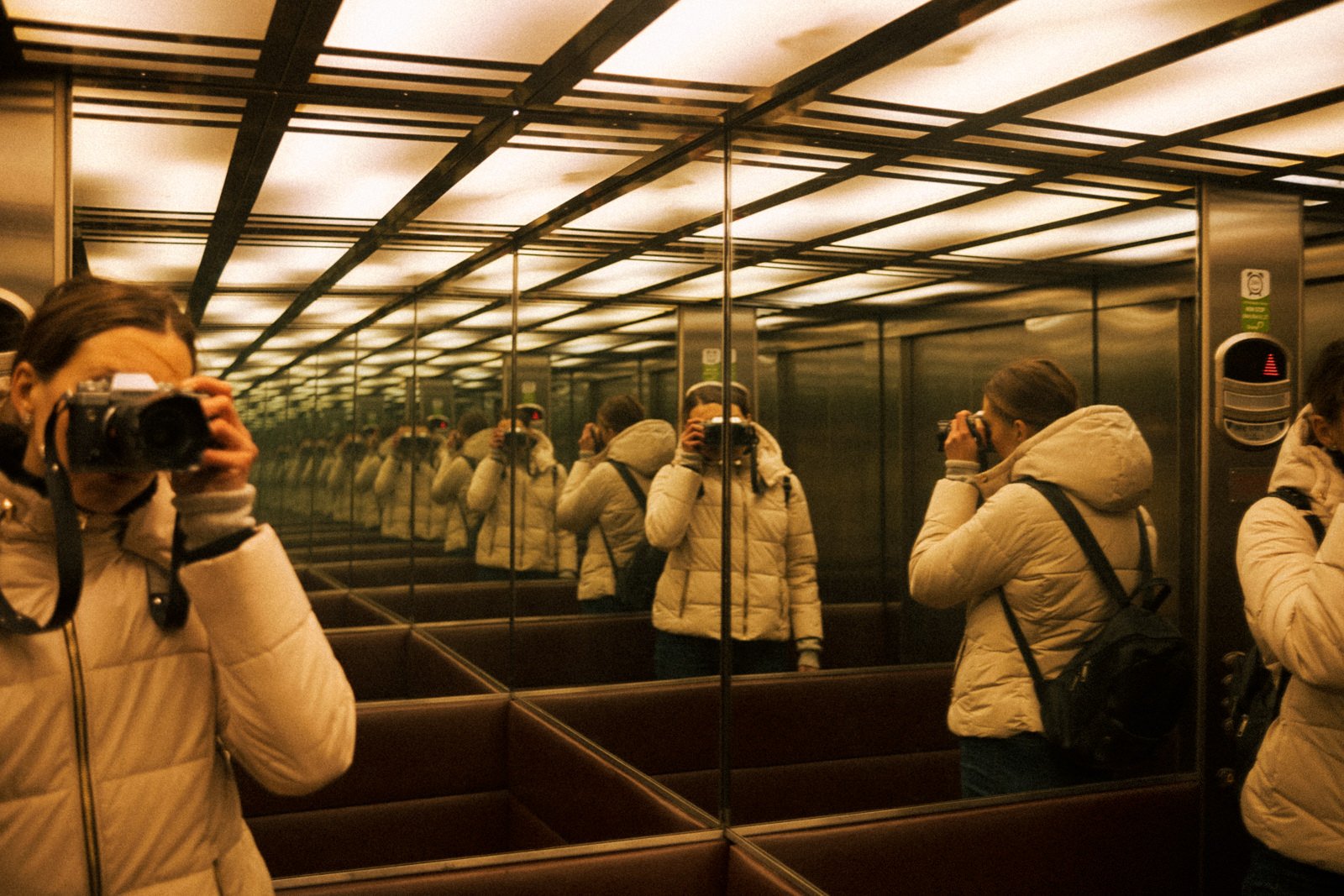 Une femme photographe dans un ascenseur capturant son reflet.