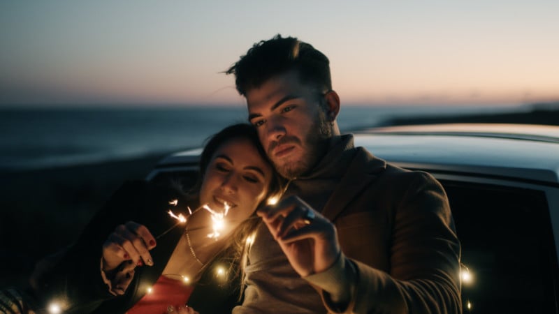 A portrait of a couple holding sparklers in a boat captured during blue hour