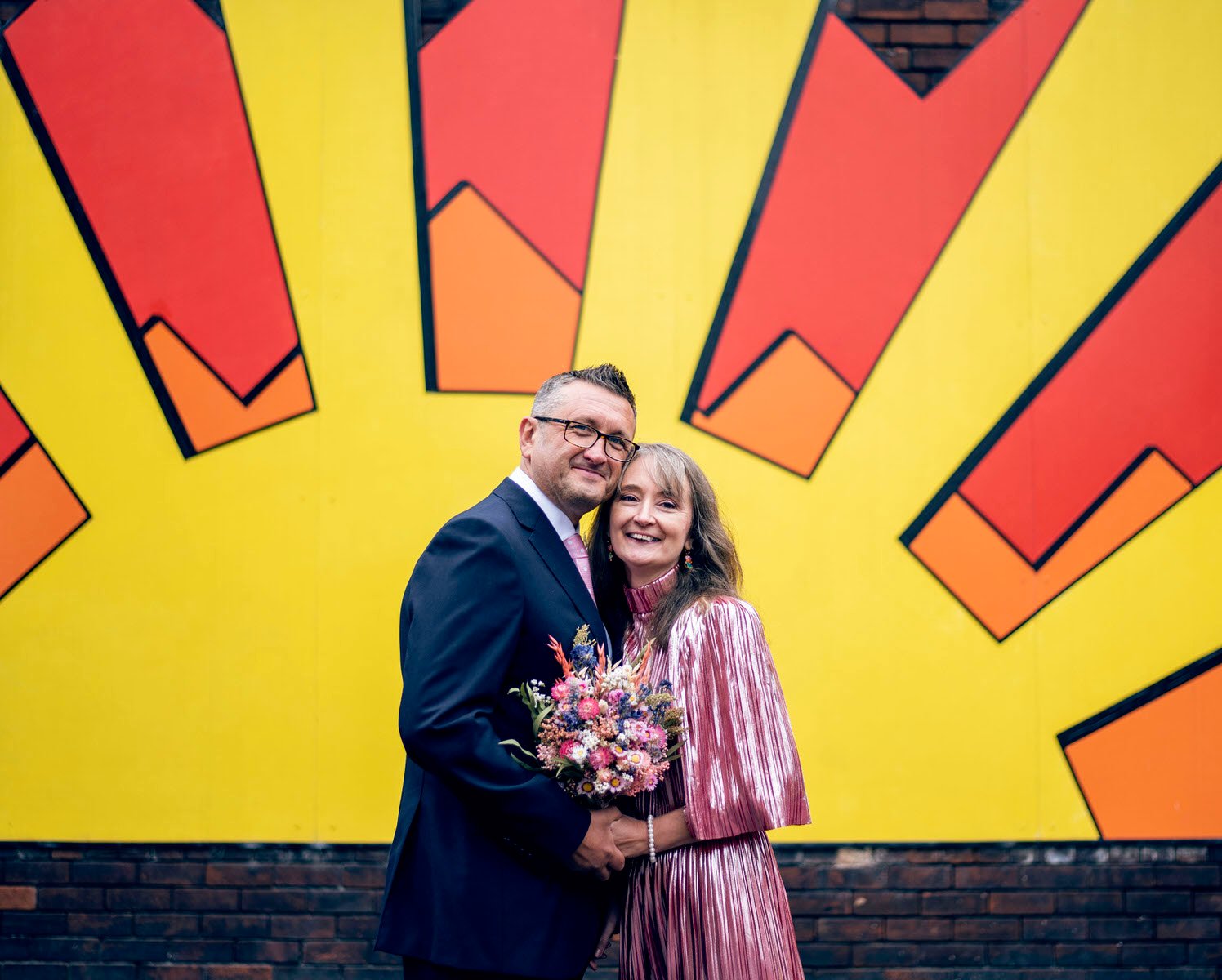 A married couple in front of a bright sunset graffiti wall