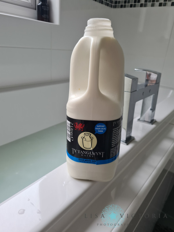 A bottle of milk on the edge of a bathtub for milk bath photography