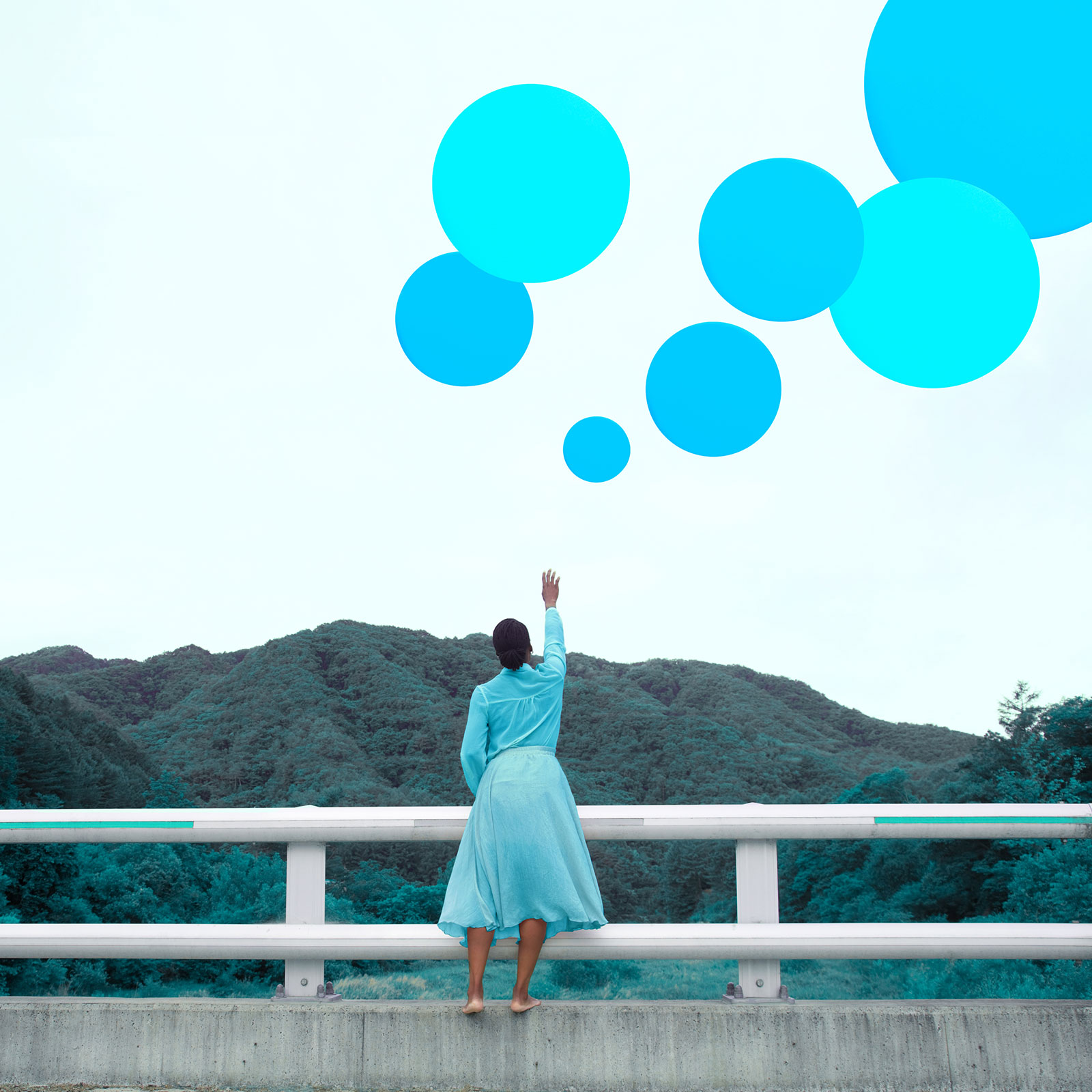 Woman reaching up to the sky, towards bright blue balloons