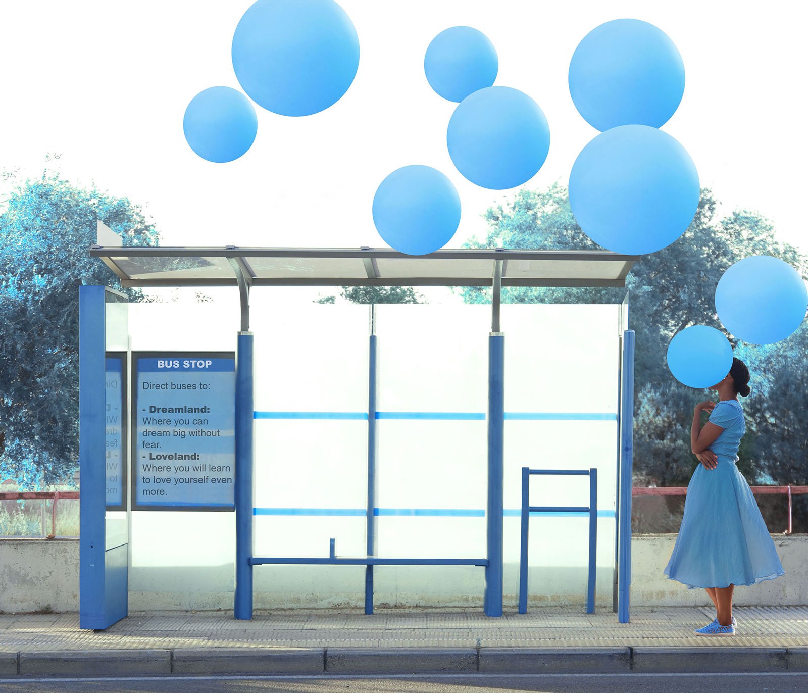 Woman at a bus stop with bright blue balloons flying overhead