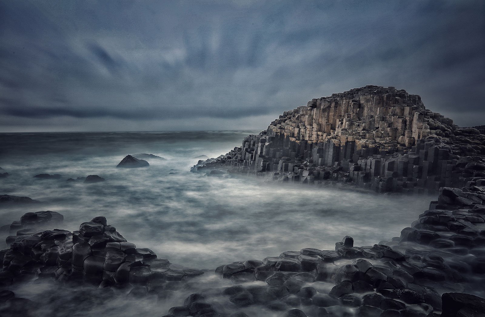 grey, blue and white waves crashing on rock towards a large stone like structure