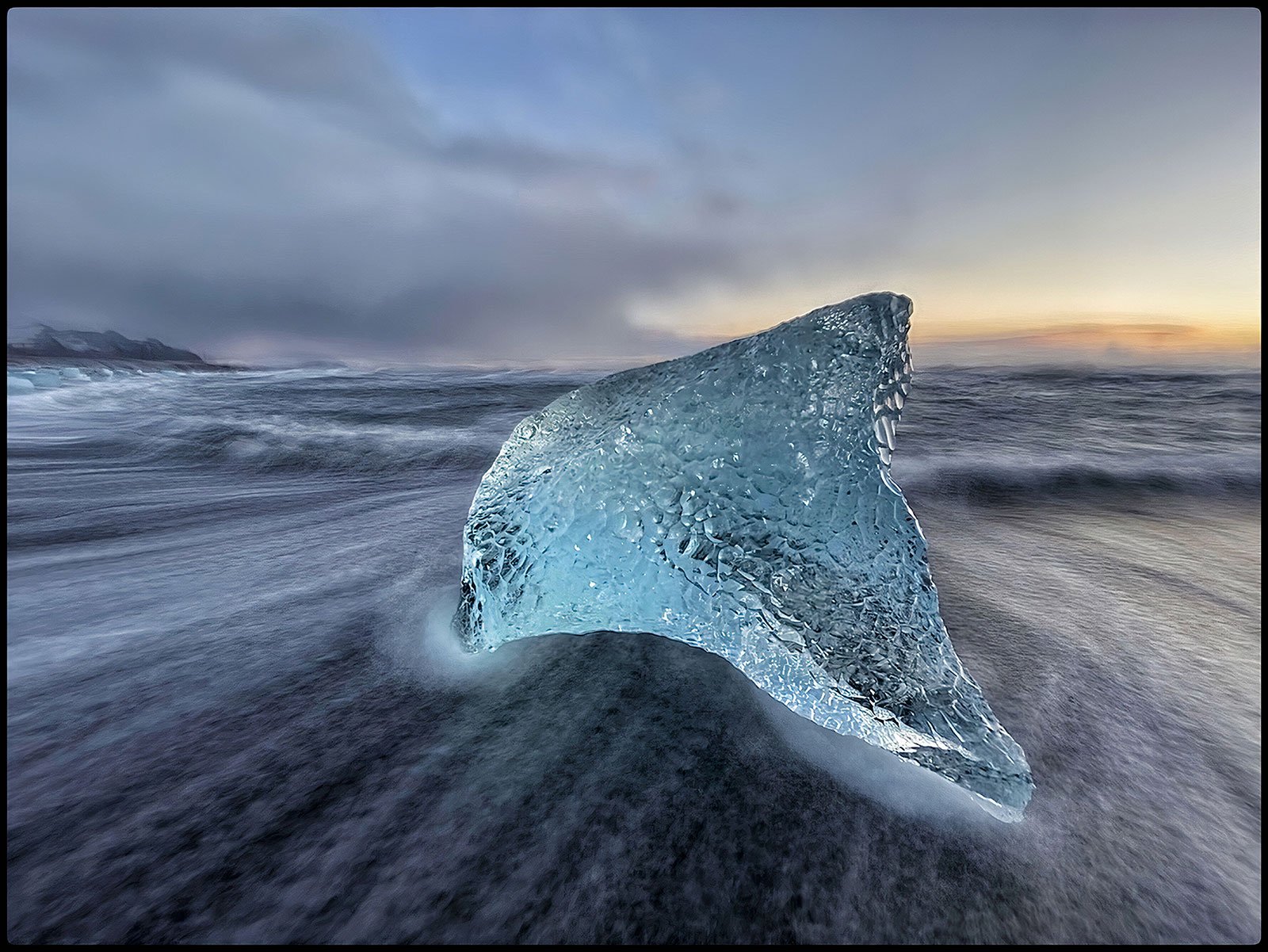 Glassy light blue iceberg and sun rise in the distance