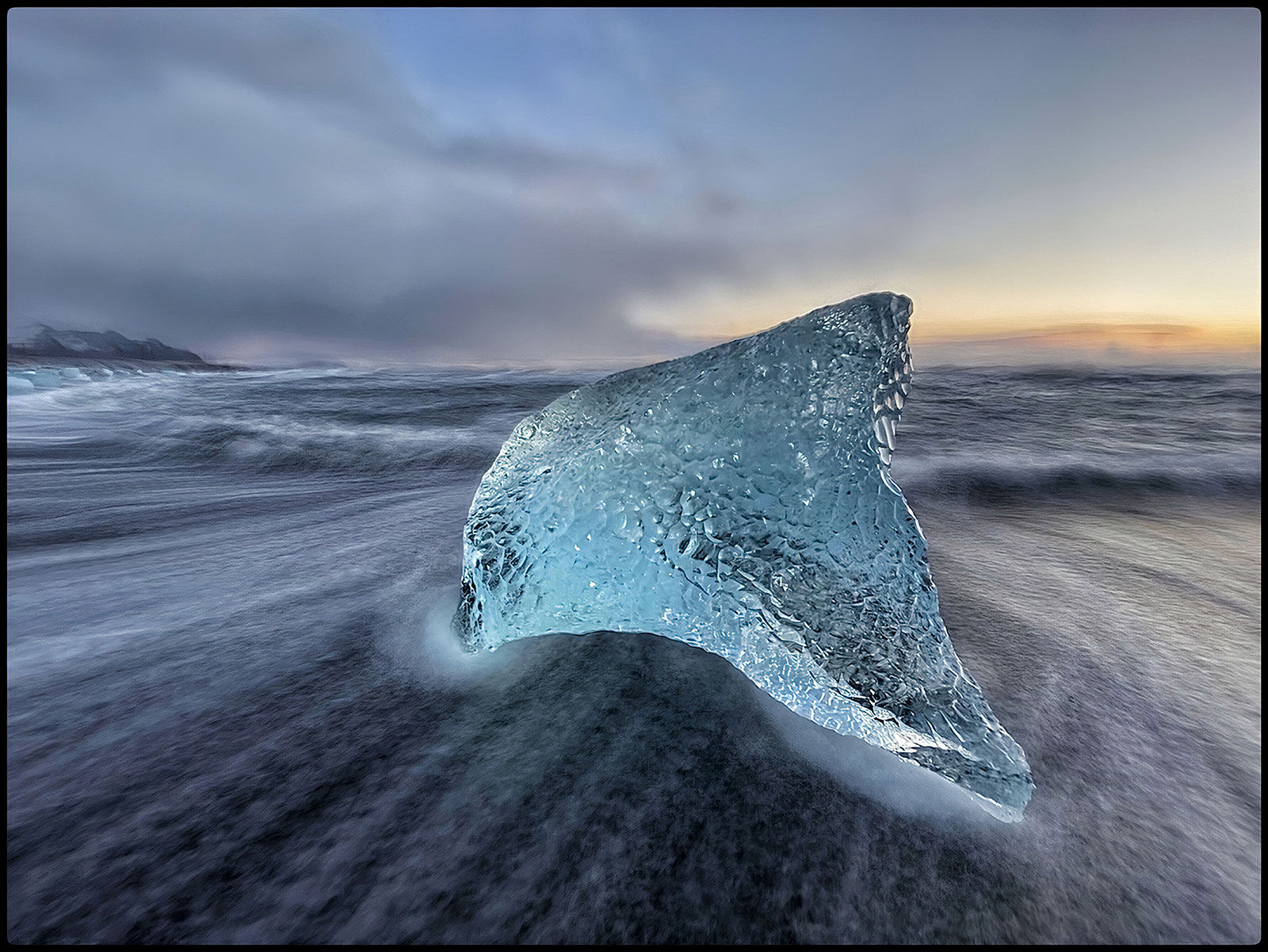 Glassy light blue iceberg and sun rise in the distance