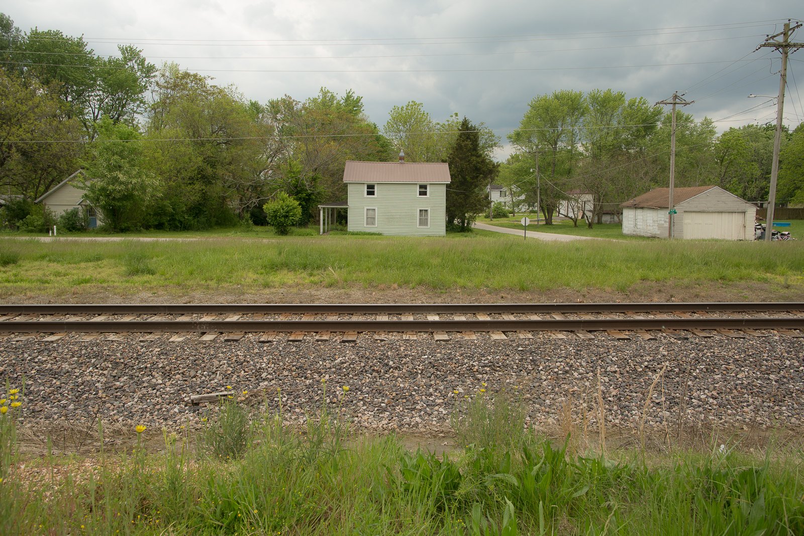 Railroad track with a white house and pink roof and cloudy sky in the distance