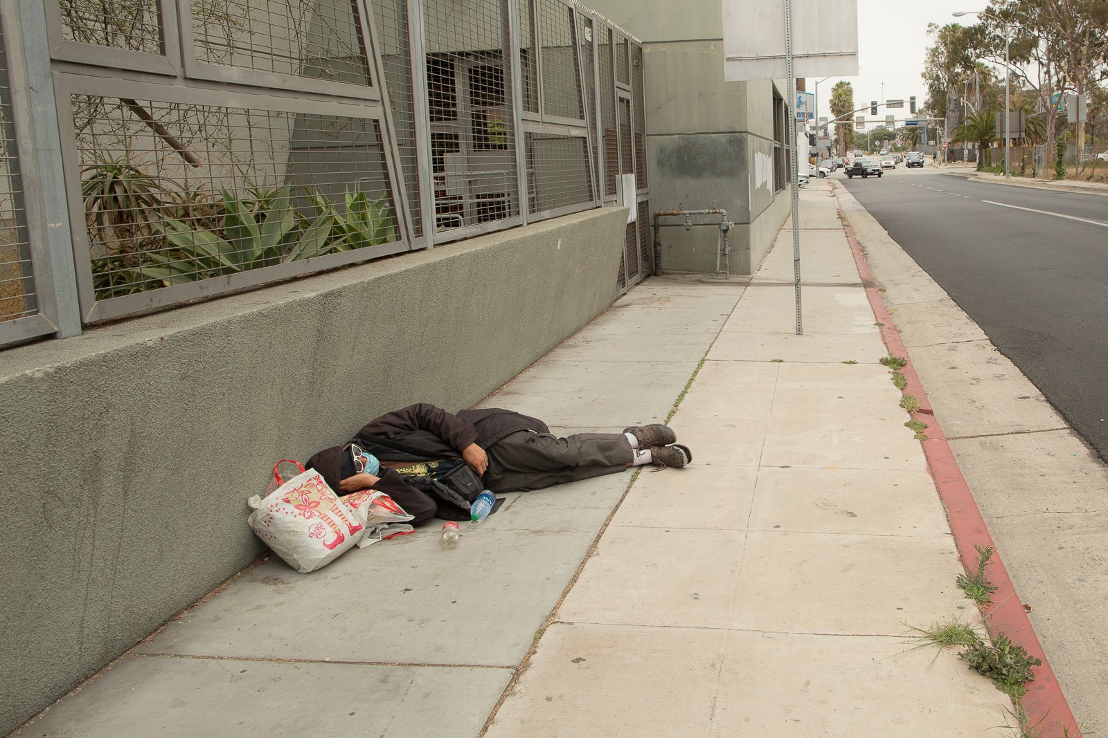A man sleeping on the sidewalk , next to a new looking building