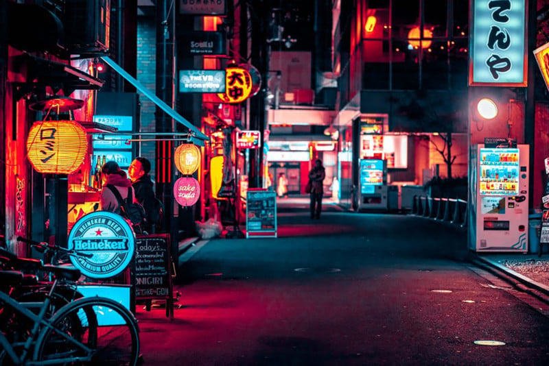 Street shot of Kyoto at night teal and red and yellow lite shopping district, people at food stalls, and and empty roadway 