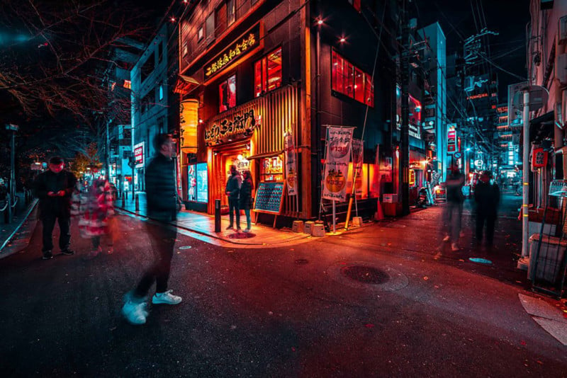 Street shot of Kyoto at night" long exposure teal and red lights with a man on the side walk at the corner of a shop