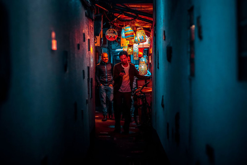 Street shot of Kyoto at night: two men, one middle-aged, one older walking down a narrow lantern lit alleyway