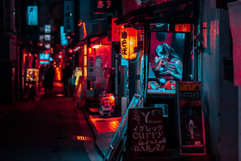 Street shot of Kyoto at night: young woman eating at a small booth, lit by a neon blue light