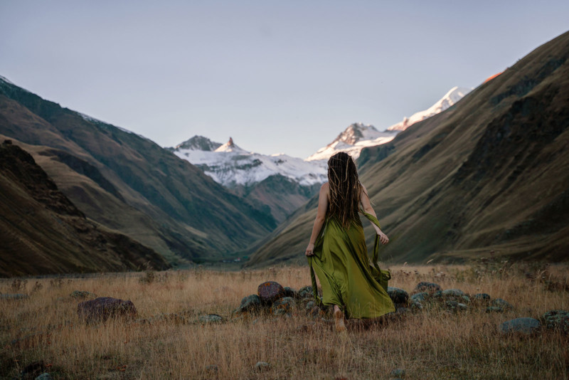 Woman in grassy fields, with mountains in the distance