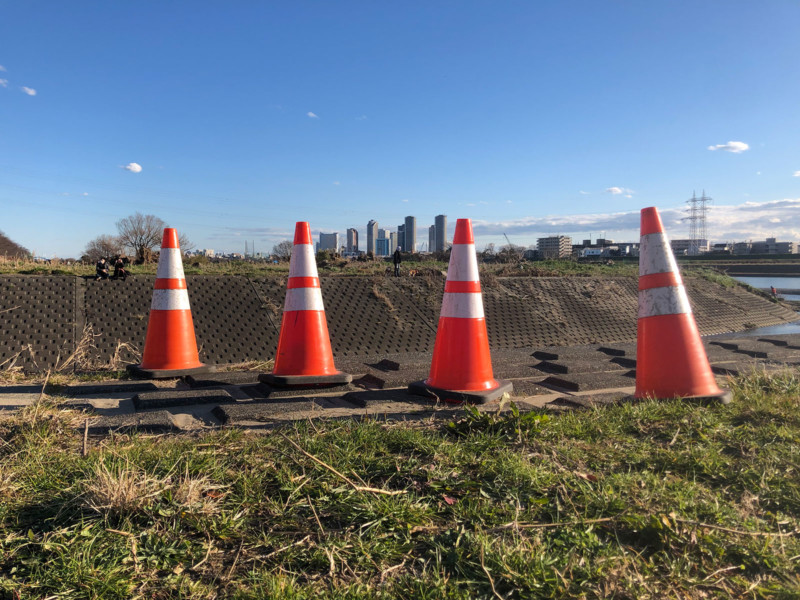 standard traffic cones in a line , with a city skyline in the distance