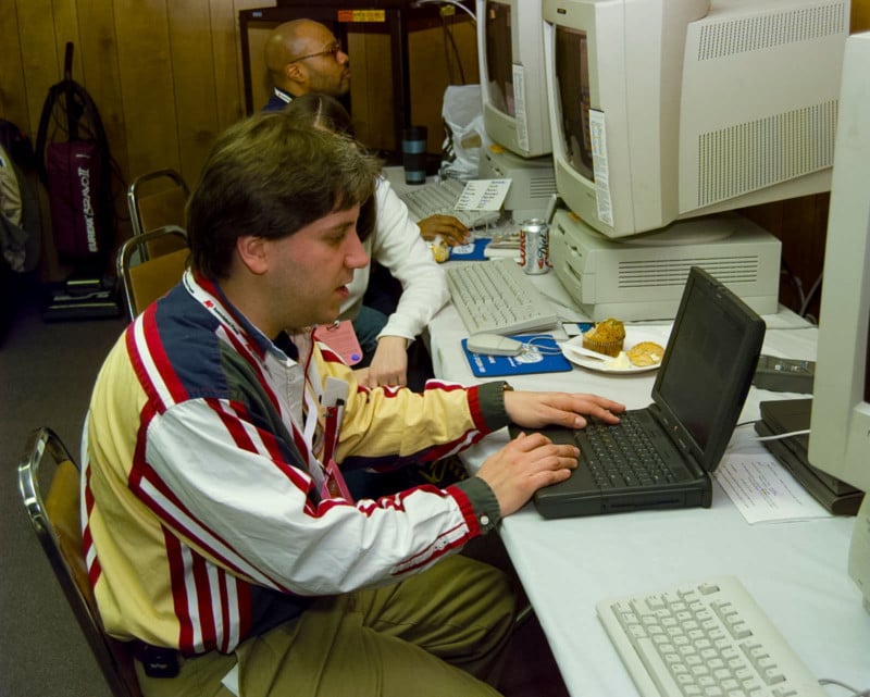 A man in a colorful shirt sits at a vintage computer laptop