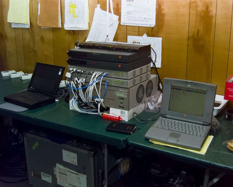 Vintage computer equipment placed on a folding table in front of a wood-paneled wall with taped-up notes.