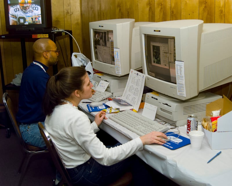 Two people sit at large computer workstations