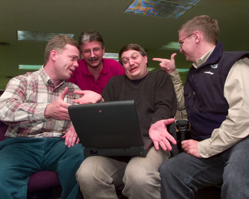 Four men gathered around a laptop computer gesturing animatedly