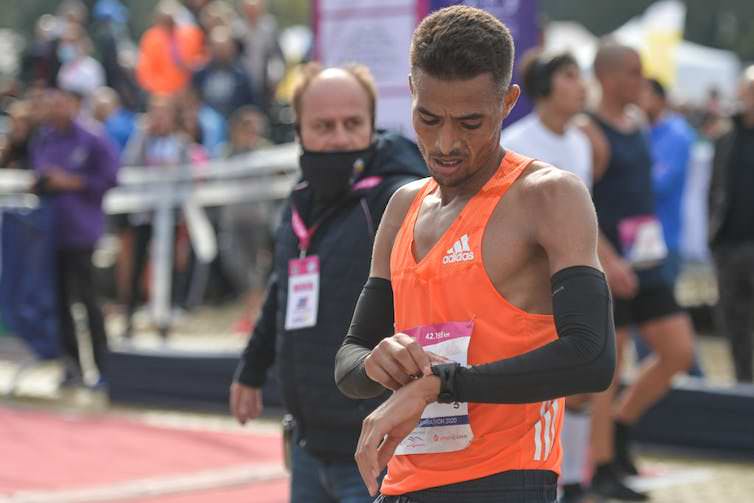 Runner wearing orange pinnie checks watch