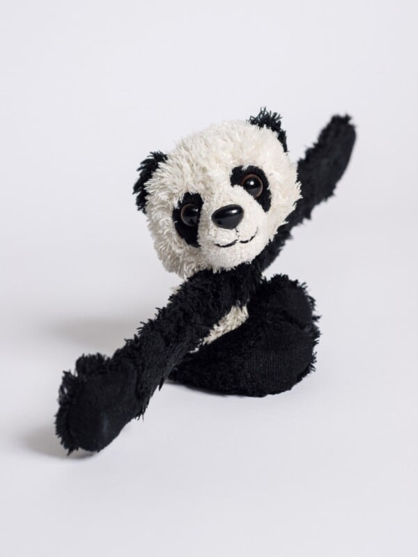 black and white panda stuffed animal sitting with stretched arms against plain white background 