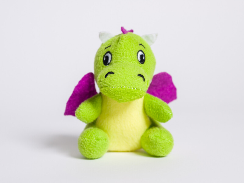 Dragon with purple wings stuffed animal sitting against plain white background 