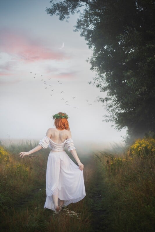 woman with red hair, and a crown of leaves holding the corner of dress while looking into a misty field 