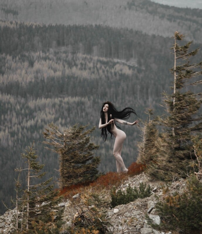Pale woman with black hair, standing on rock hill,