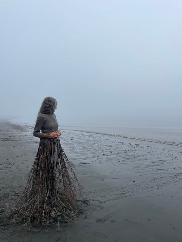 A moody image with a woman wearing a skirt made from twigs. 