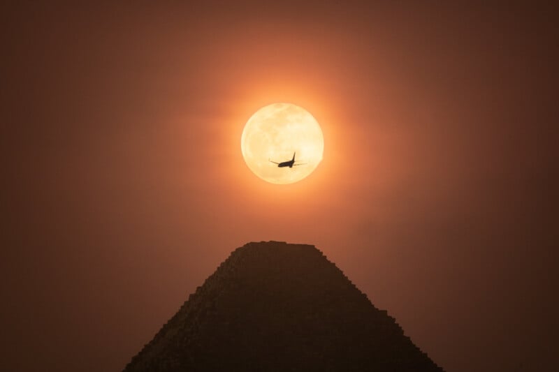 An airplane silhouetted against the Moon above the Great Pyramid of Giza.