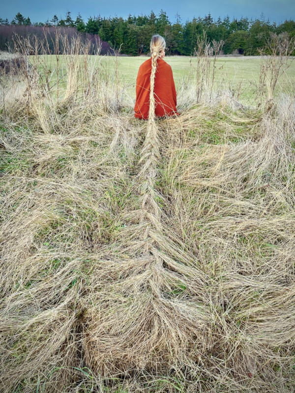 Une femme avec ses cheveux apparemment tissés dans l'herbe longue. 