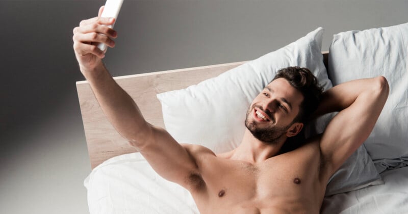 Shirtless man takes a selfie while lying in bed.